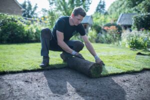Man rolt grasmatten uit op voorbereide grond tijdens het aanleggen van een gazon