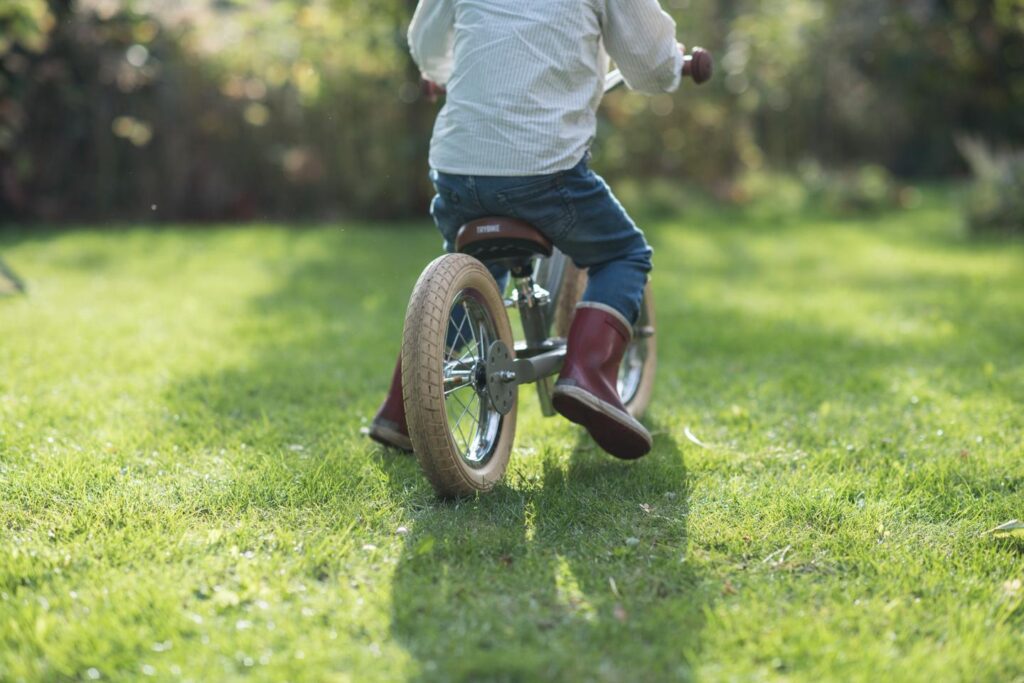 Kind op fiets rijdt over groene grasmatten in tuin