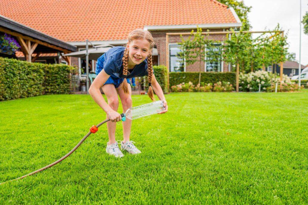 Kind test sproeier van fles en slang op grasmatten