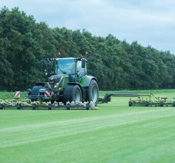 Een grote EcoClipper grasmaaier achter een tractor die duurzaam grasmatten maait op een teeltveld