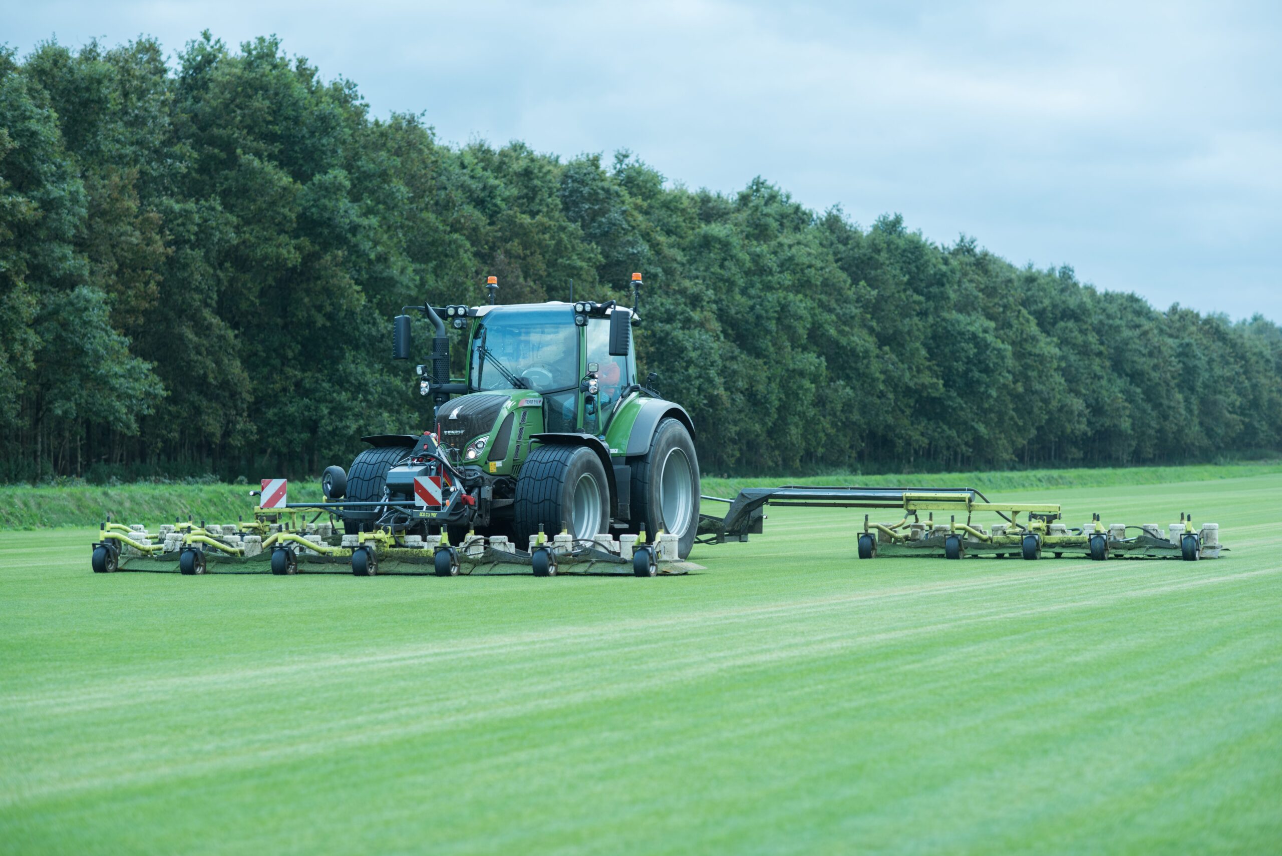 Een grote EcoClipper grasmaaier achter een tractor die duurzaam grasmatten maait op een teeltveld