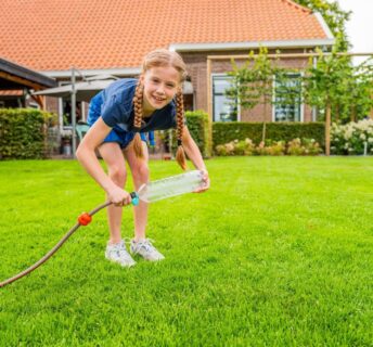 Kind test sproeier van fles en slang op grasmatten