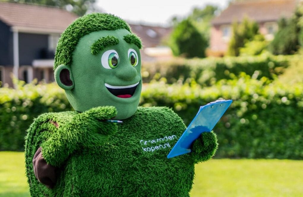 Mascotte Grasmattie met clipboard geeft tips voor het leggen van grasmatten