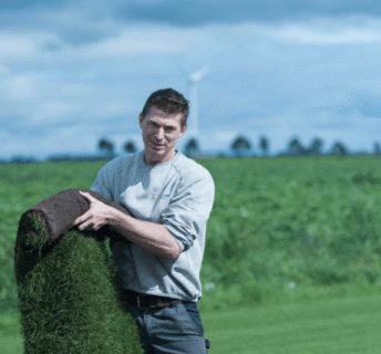 Medewerker van een grasmattenbedrijf houdt een rol grasmatten vast op het veld