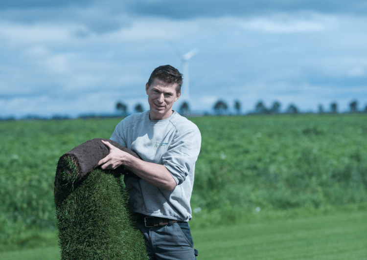 Medewerker van een grasmattenbedrijf houdt een rol grasmatten vast op het veld