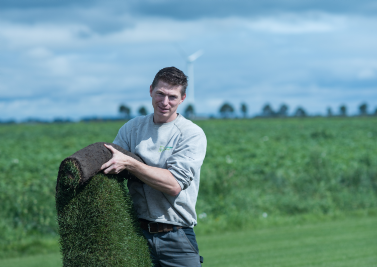 Medewerker van een grasmattenbedrijf houdt een rol grasmatten vast op het veld