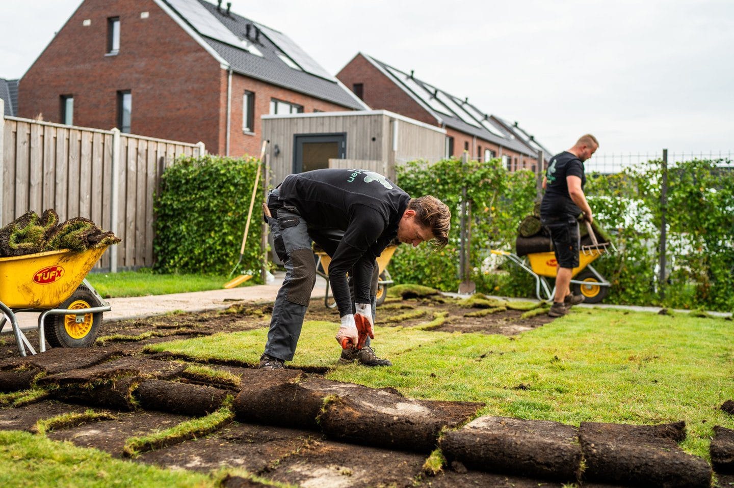 Twee tuiniers leggen samen grasmatten aan in een tuin